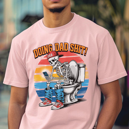 May include: Pink t-shirt with a graphic of a skeleton wearing a red cap and blue jeans, sitting on a toilet while using a smartphone. The text "DOING DAD SHIT!" is above the graphic.