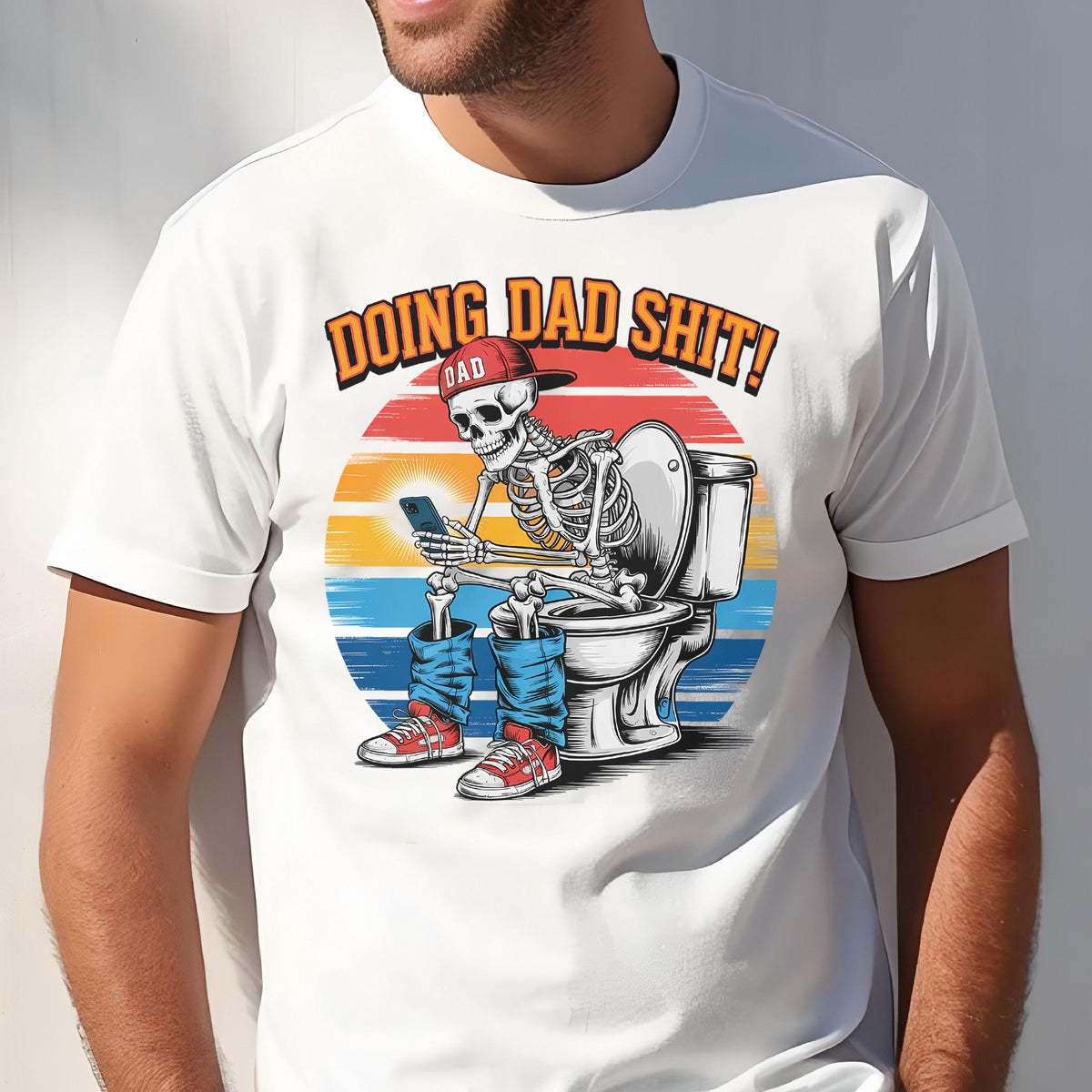 May include: White t-shirt with a graphic of a skeleton wearing a red cap and blue jeans, sitting on a toilet while looking at a phone. The text "DOING DAD SHIT!" is above the skeleton, with a sunset background.