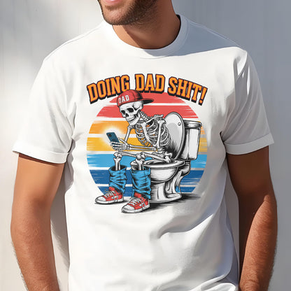 May include: White t-shirt with a graphic of a skeleton wearing a red cap and blue jeans, sitting on a toilet while looking at a phone. The text "DOING DAD SHIT!" is above the skeleton, with a sunset background.