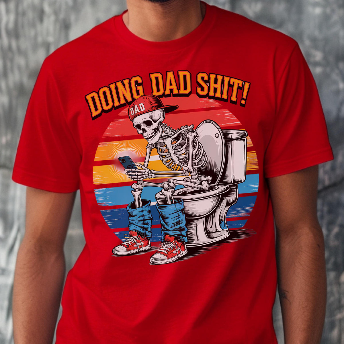 May include: Red t-shirt with a graphic of a skeleton wearing a "DAD" cap, blue jeans, and red sneakers, sitting on a toilet while looking at a phone. The text "DOING DAD SHIT!" is above the skeleton, set against a sunset background.
