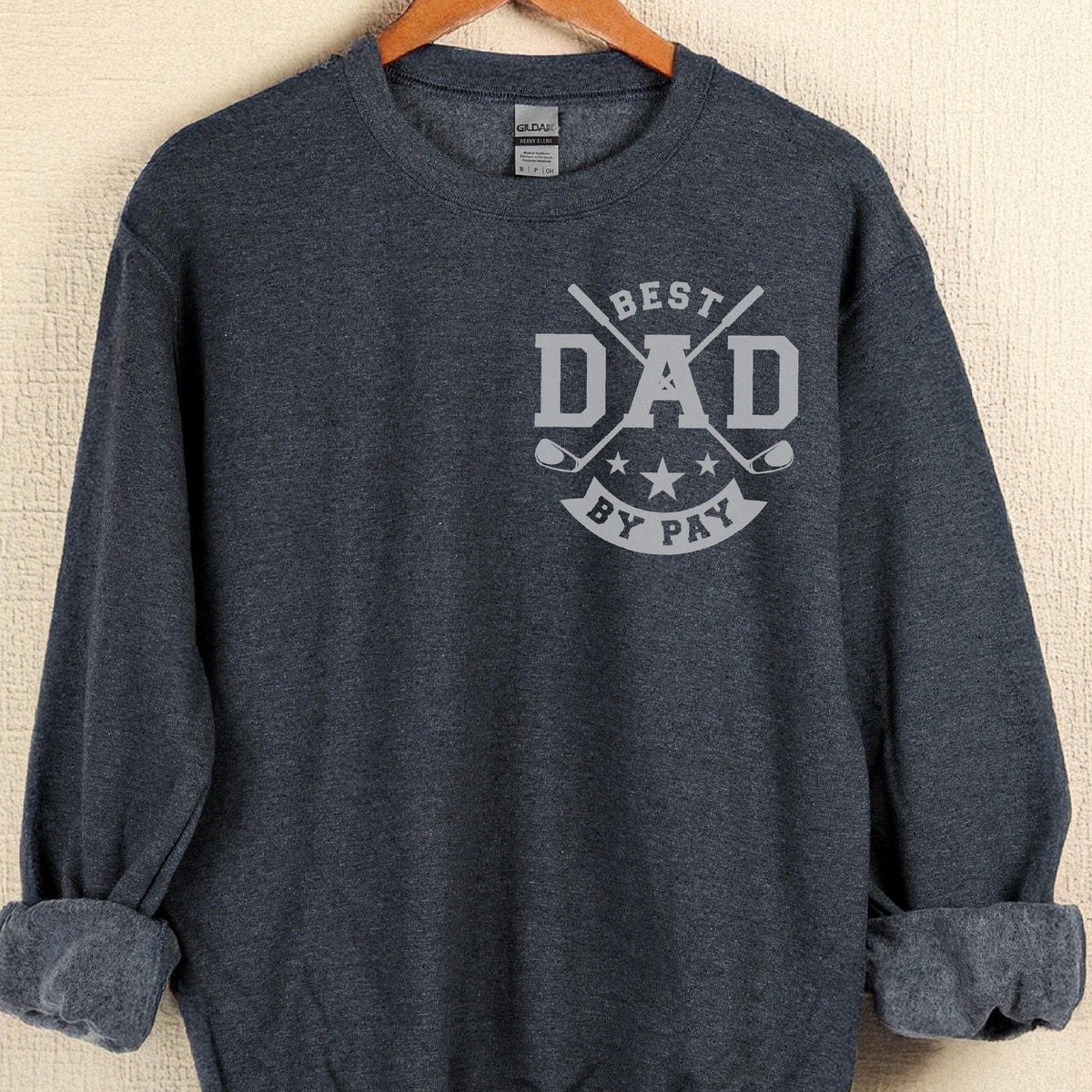 May include: A navy blue sweatshirt with the text "BEST DAD BY PAY" in gray. The design includes crossed golf clubs and stars. The sweatshirt is hanging on a wooden hanger.