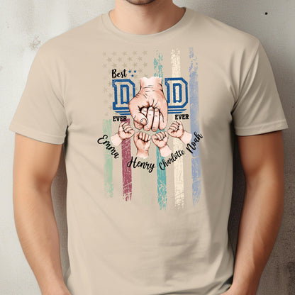 May include: Beige t-shirt with a graphic design featuring the words "Best Dad Ever" in blue, a fist, and the names Emma, Henry, Charlotte, and Noah. The design includes a distressed American flag.