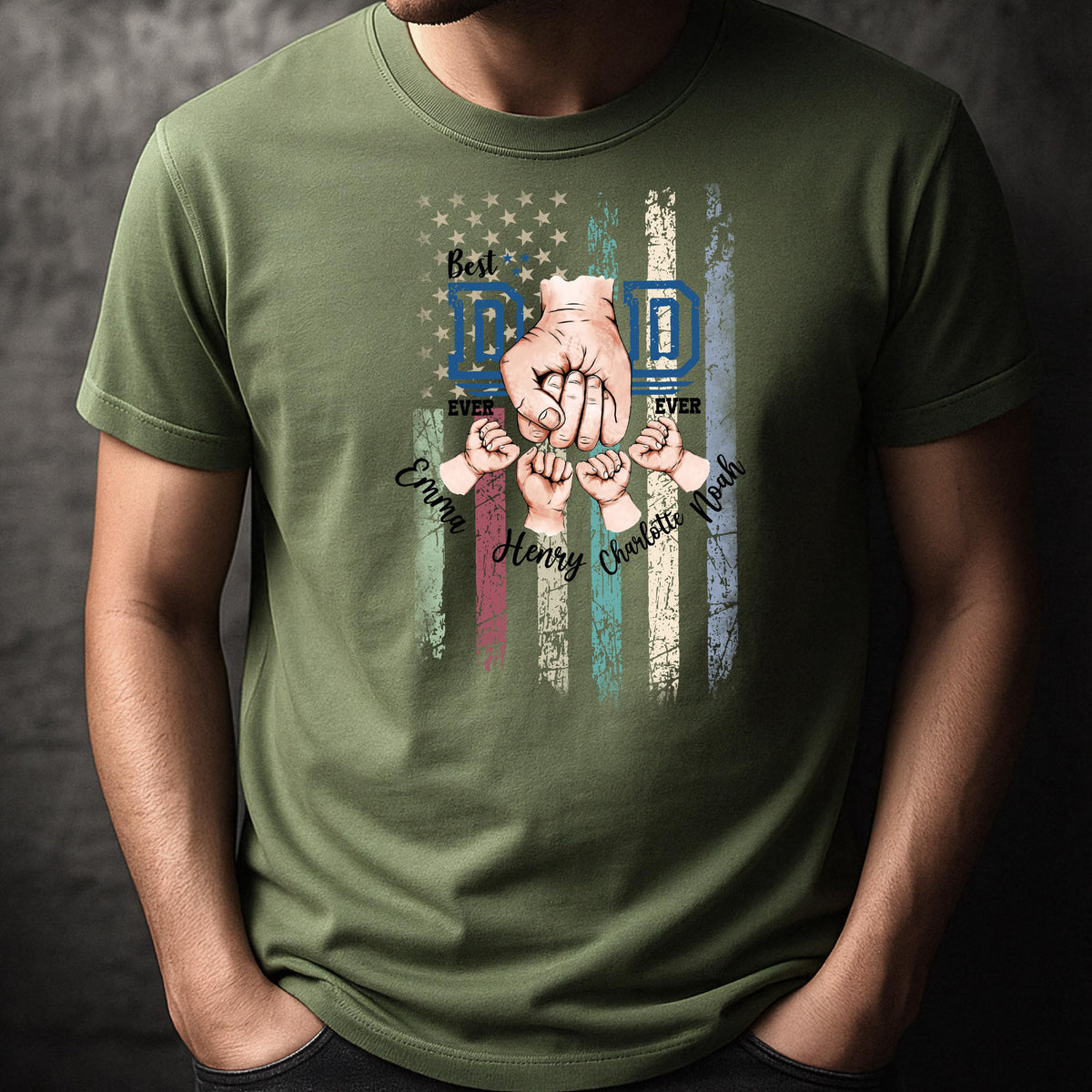 May include: Olive green t-shirt featuring a graphic design with a patriotic flag motif. The design includes the words "Best Dad Ever" and the names "Emma, Henry, Charlotte, Noah". The design also features a fist and several smaller hands.