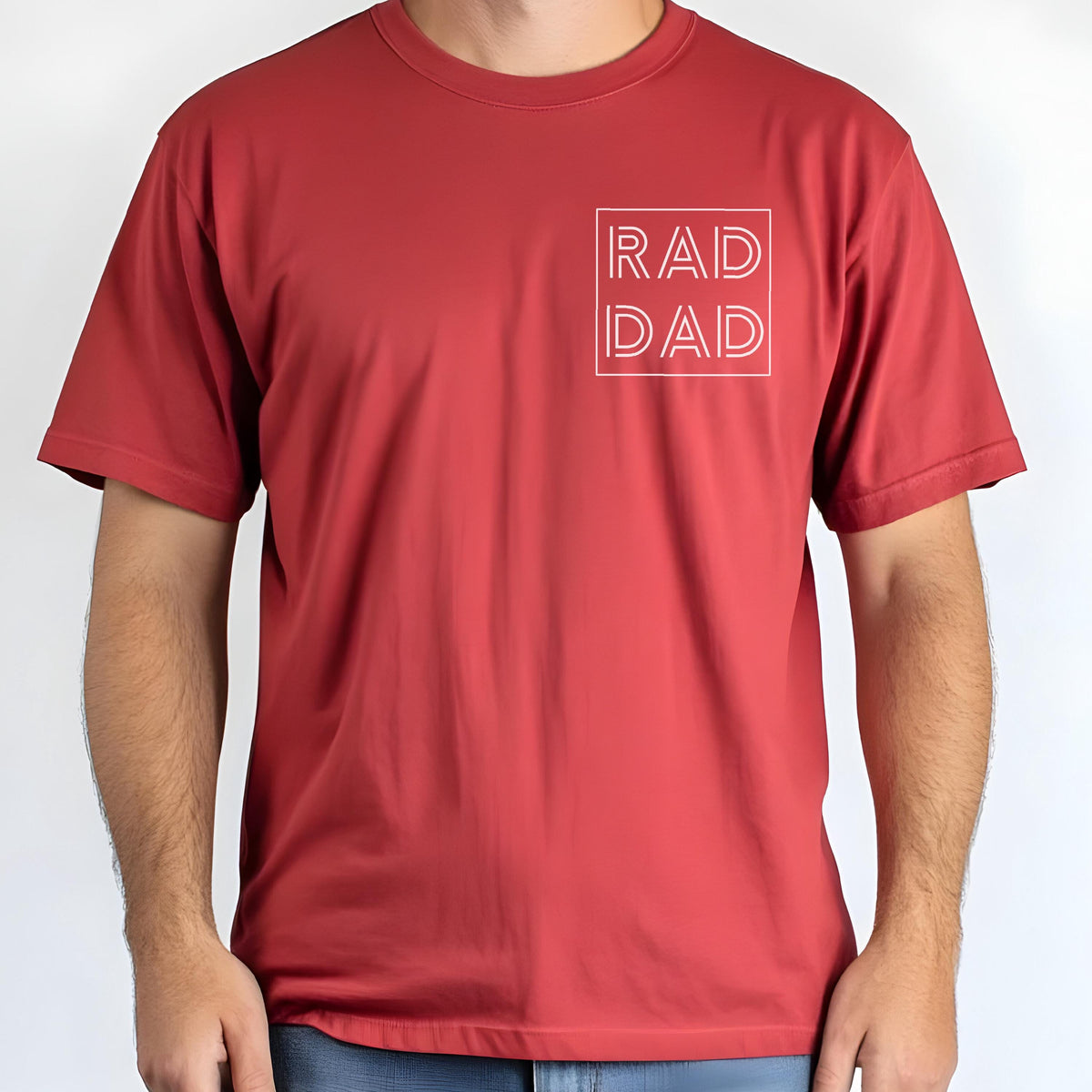 May include: A red t-shirt with the text "RAD DAD" in a white square on the upper left chest. The shirt has short sleeves and a crew neck. The fabric appears to be a lightweight, breathable material.
