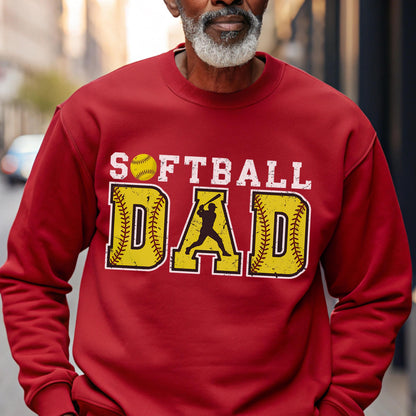 May include: A red sweatshirt with the words "SOFTBALL DAD" in white and yellow. The word "SOFTBALL" is above the word "DAD". The letter "D" in "DAD" has a silhouette of a batter swinging a bat.