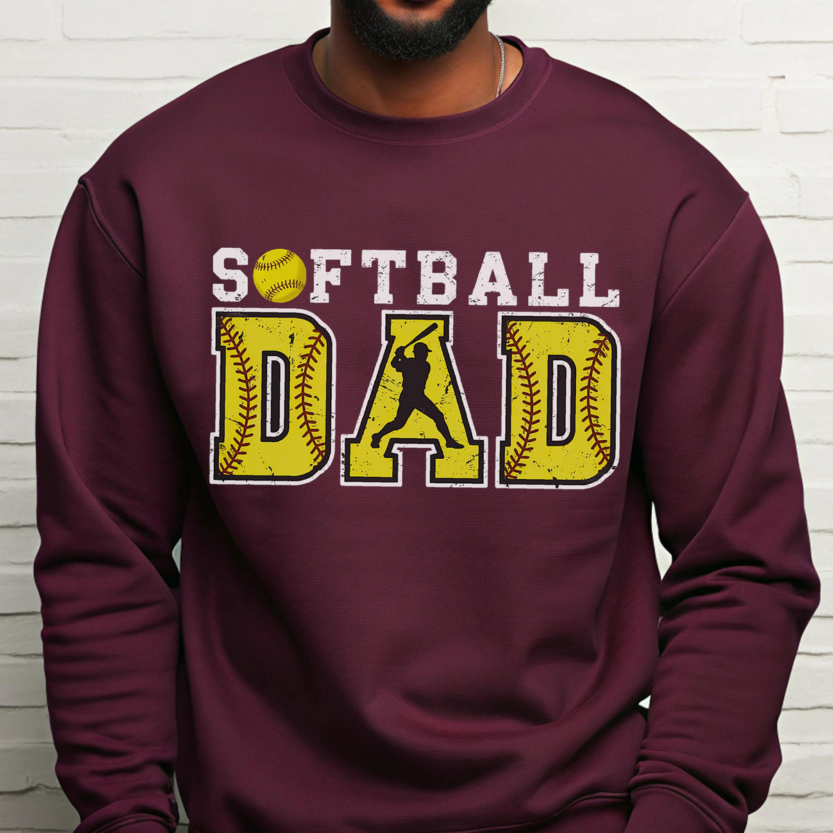 May include: Burgundy sweatshirt with the words "SOFTBALL DAD" in white and yellow. The word "DAD" is designed with a softball and a batter silhouette. The sweatshirt is a solid burgundy color.