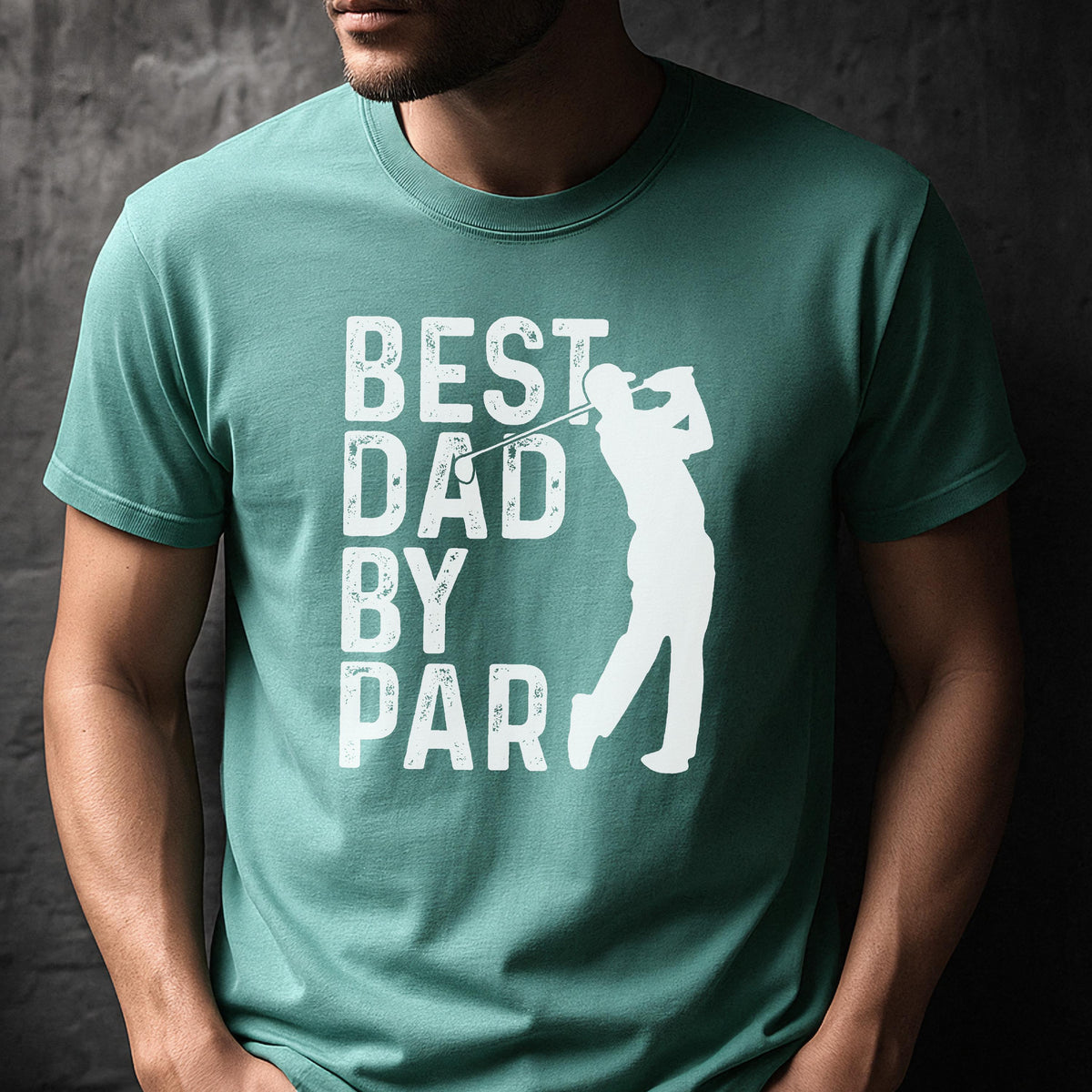 May include: A teal short-sleeved crew neck t-shirt featuring a white graphic print. The design includes the text "BEST DAD BY PAR" stacked vertically on the left, next to a white silhouette of a golfer mid-swing with a golf club.