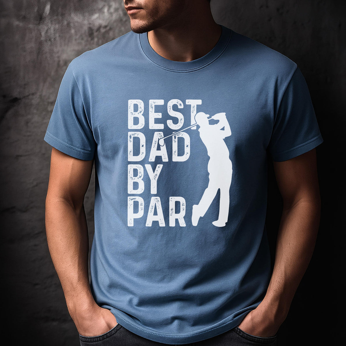 May include: A dusty blue short-sleeved t-shirt featuring a white graphic print. The design includes the text "BEST DAD BY PAR" in a distressed font, accompanied by a white silhouette of a golfer mid-swing with a golf club.