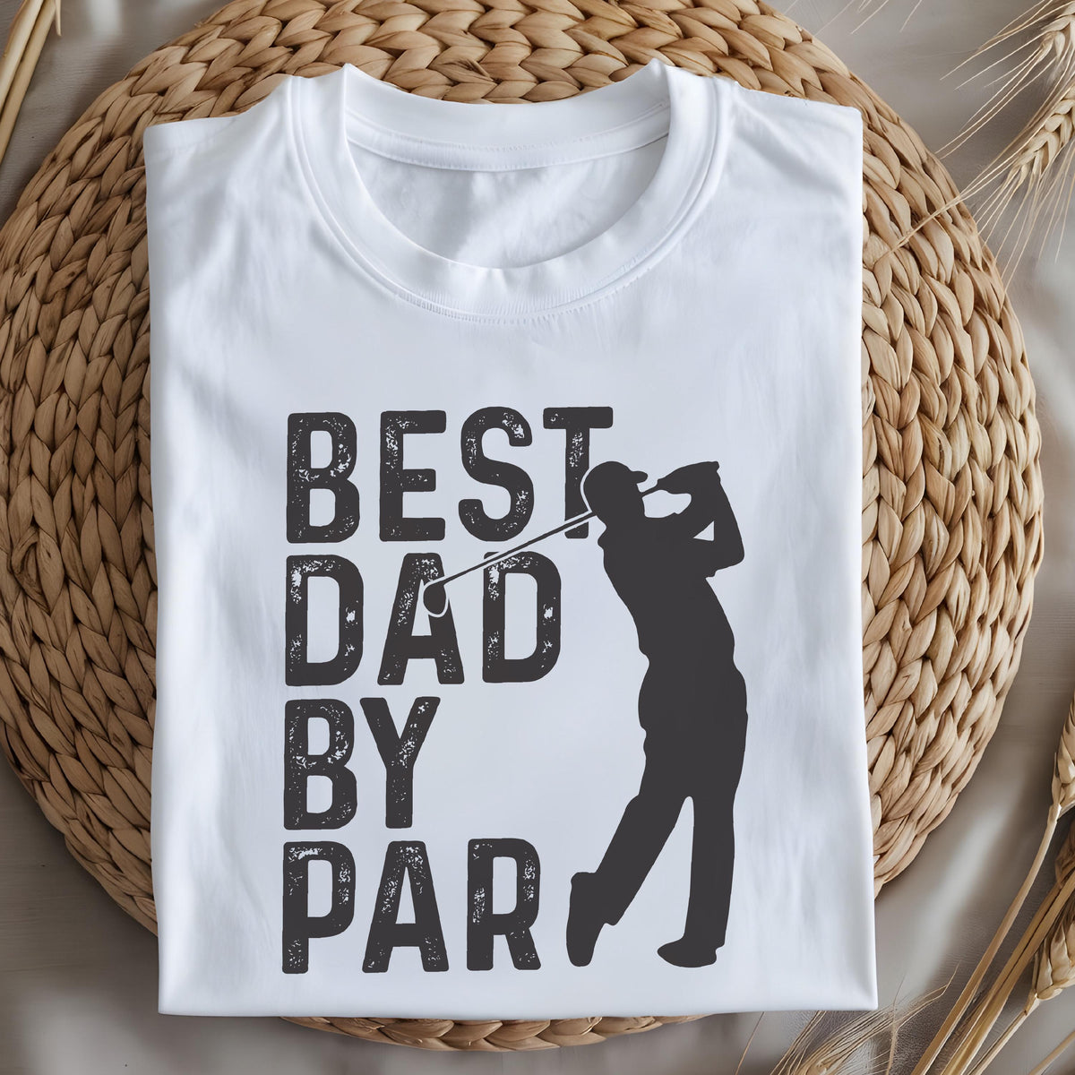 May include: A white short-sleeved t-shirt featuring a dark gray graphic print. The design includes the text "BEST DAD BY PAR" in a bold, distressed font, accompanied by a silhouette of a person swinging a golf club to complete the image.