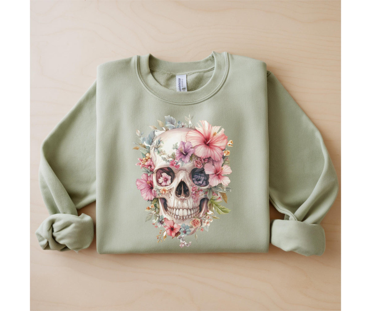 May include: Sage green sweatshirt featuring a watercolor skull design adorned with pink, purple, and yellow flowers. The skull has detailed shading and is centered on the front of the long-sleeved crew neck top.