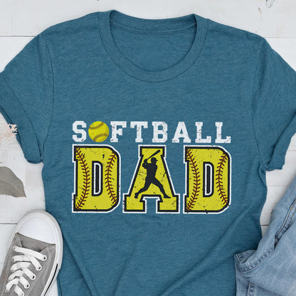 May include: Teal blue t-shirt with the text "Softball Dad" in white with a yellow softball and a silhouette of a softball player in the middle of the word "Dad".