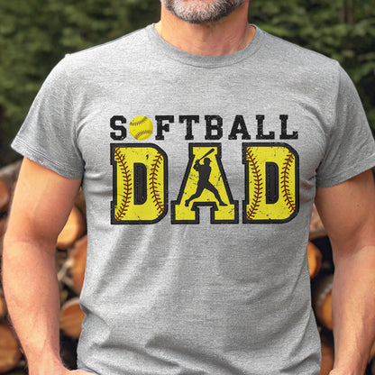 May include: A gray t-shirt with the text "SOFTBALL DAD" in yellow and black letters. A yellow softball with red stitching is above the word "SOFTBALL". A silhouette of a baseball player is in the middle of the word "DAD".
