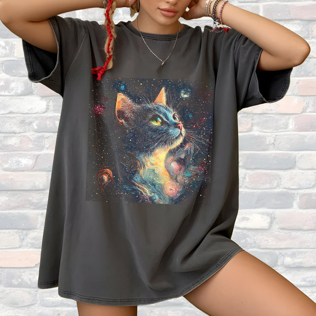 May include: Dark gray oversized t-shirt featuring a colorful illustration of a cat with a cosmic background. The cat has blue fur, green eyes, and a vibrant, swirling nebula design. The shirt has short sleeves and a relaxed fit.