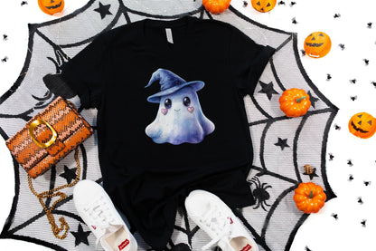 May include: Black t-shirt featuring a watercolor illustration of a friendly ghost wearing a blue witch hat. The ghost has heart-shaped cheeks. The shirt is styled with white sneakers, an orange purse, and Halloween decorations.