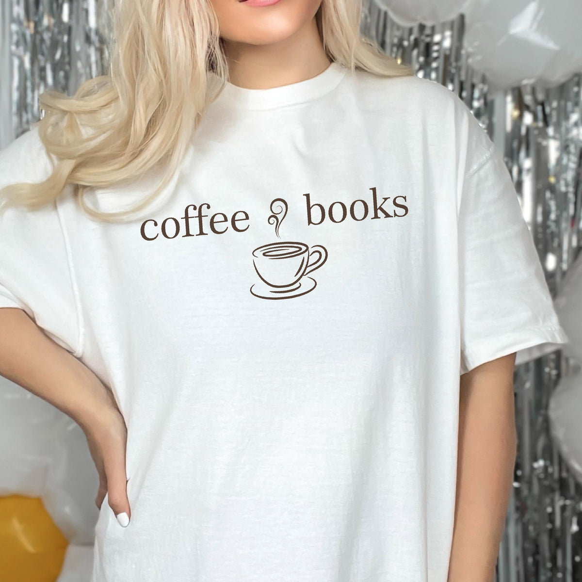 May include: A white short-sleeved t-shirt featuring the brown text coffee books with a small brown graphic of a steaming coffee cup centered between the two words. The shirt has a crew neckline and a standard fit, made of a solid white fabric.