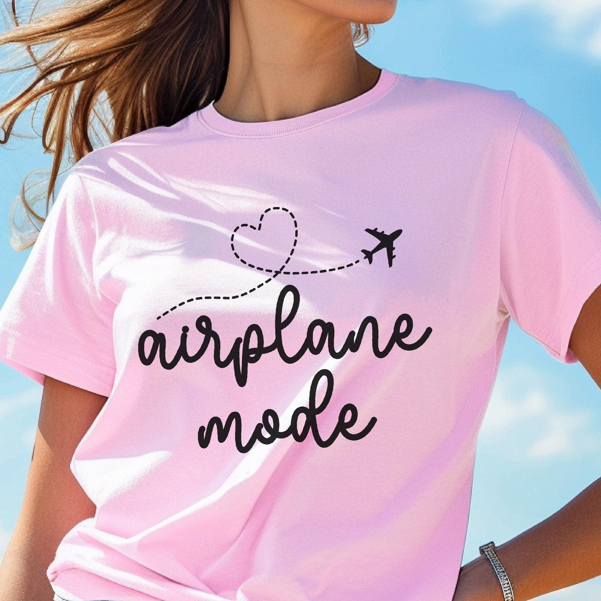 May include: A light pink t-shirt with the words "airplane mode" in a black script font. A black airplane graphic follows a dotted line from a heart shape. The shirt is short-sleeved.