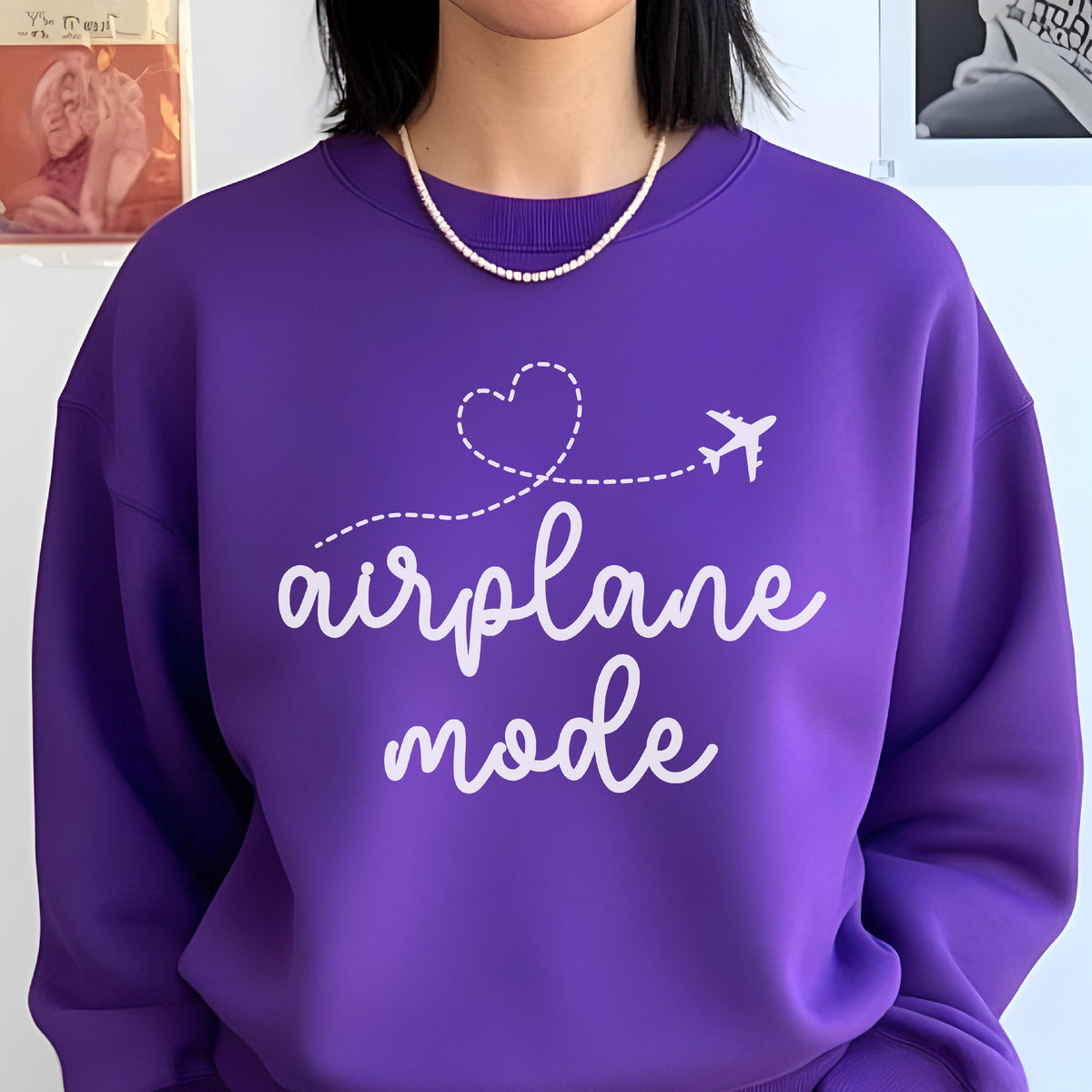 May include: A vibrant purple crewneck sweatshirt featuring a white graphic print on the chest. The design includes a small airplane silhouette with a dashed line forming a heart shape above the white cursive text that reads airplane mode.