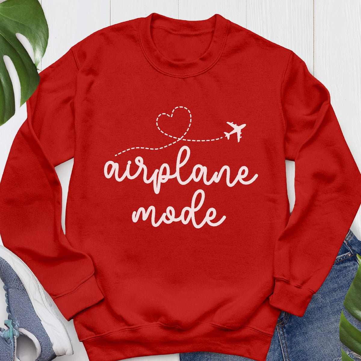 May include: A bright red long-sleeve crewneck sweatshirt featuring white text that reads airplane mode. Above the text is a white dashed line forming a heart shape that ends with a small airplane icon. The sweatshirt has ribbed cuffs and a ribbed neckline.