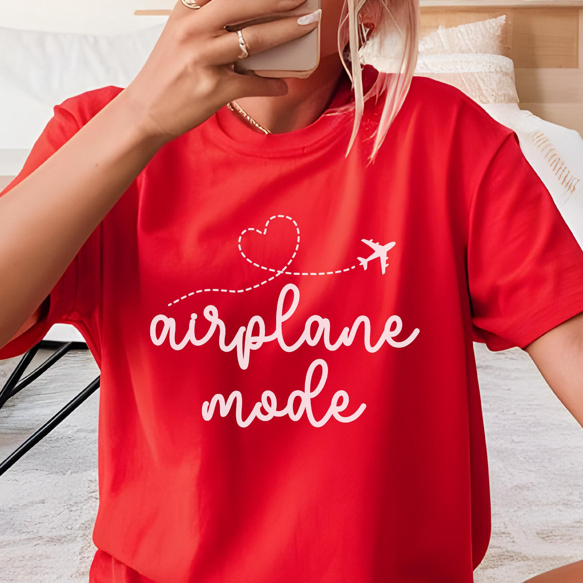 May include: A bright red t-shirt with the words "airplane mode" in a white script font. A white dotted line with a heart and airplane graphic is above the text. The shirt is short-sleeved and made of a soft material.