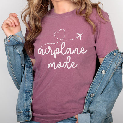 May include: Mauve t-shirt with the words "airplane mode" in white script. A white airplane graphic and a heart-shaped dotted line are above the text. The person is wearing a denim jacket.
