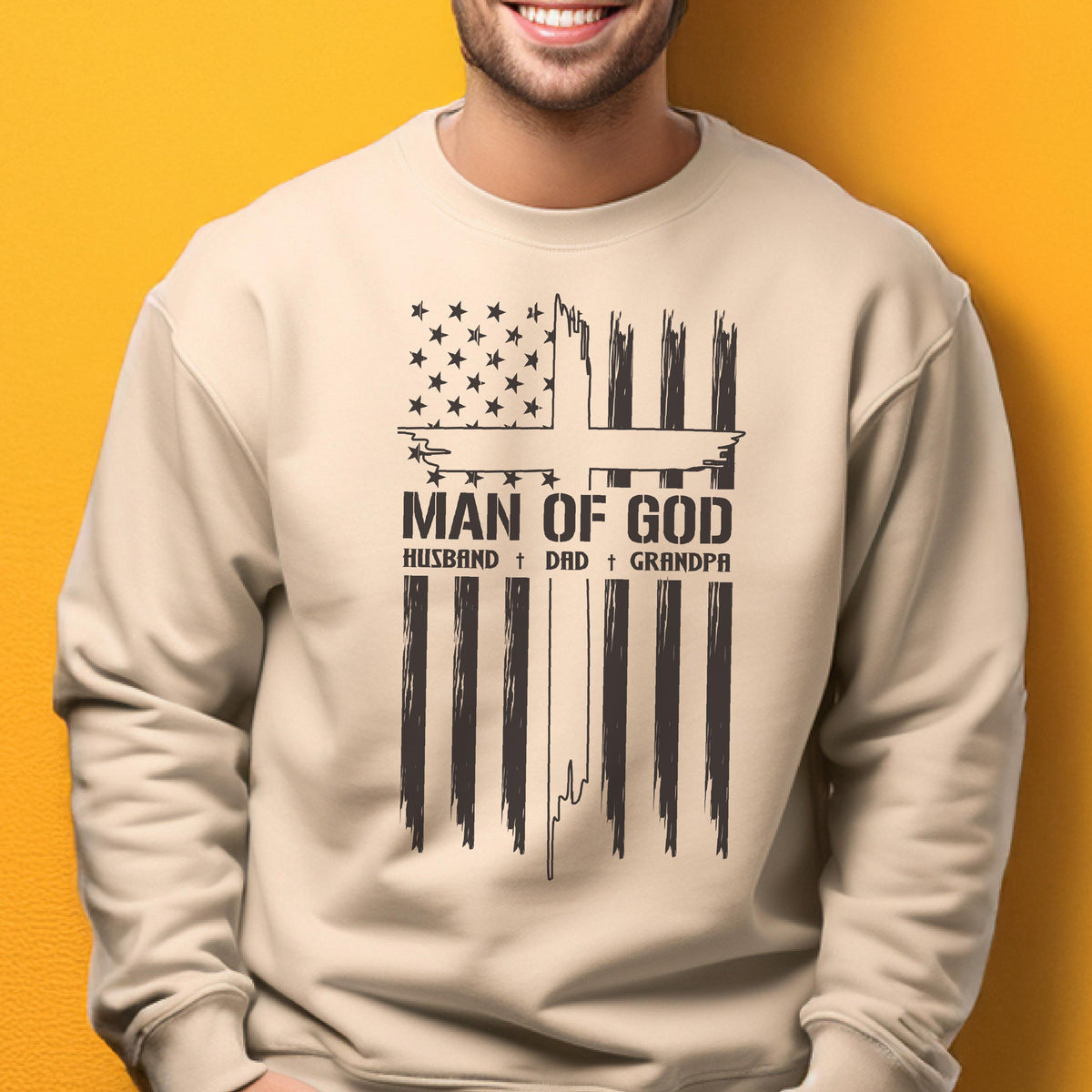 May include: A beige sweatshirt with a black graphic design. The design features a stylized American flag with the text "MAN OF GOD" and the words "HUSBAND + DAD + GRANDPA" below it. The sweatshirt is a casual style.