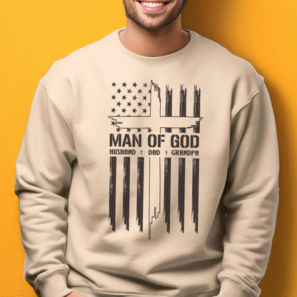 May include: A beige sweatshirt with a black graphic design. The design features a stylized American flag with the text "MAN OF GOD" and the words "HUSBAND + DAD + GRANDPA" below it. The sweatshirt is a casual style.