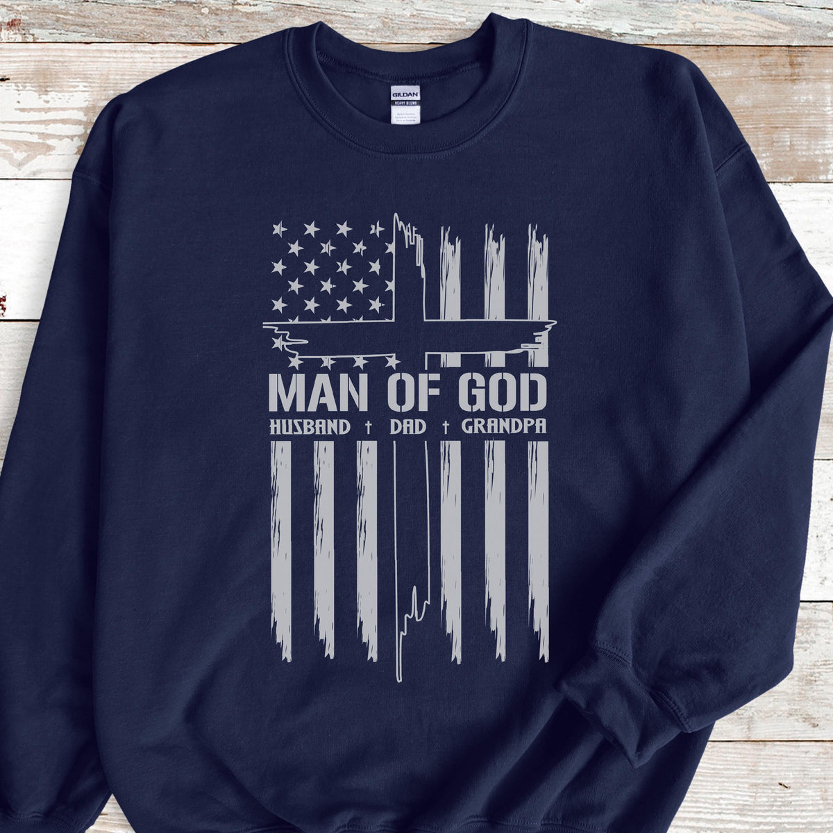 May include: Navy blue sweatshirt with a distressed white graphic resembling an American flag and the words "MAN OF GOD." Below the main text are the words "HUSBAND + DAD + GRANDPA."