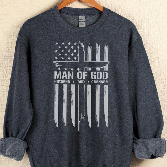 May include: Dark navy blue sweatshirt with a distressed white graphic. The graphic features an American flag design with the text "MAN OF GOD" and the words "HUSBAND + DAD + GRANDPA" below it.