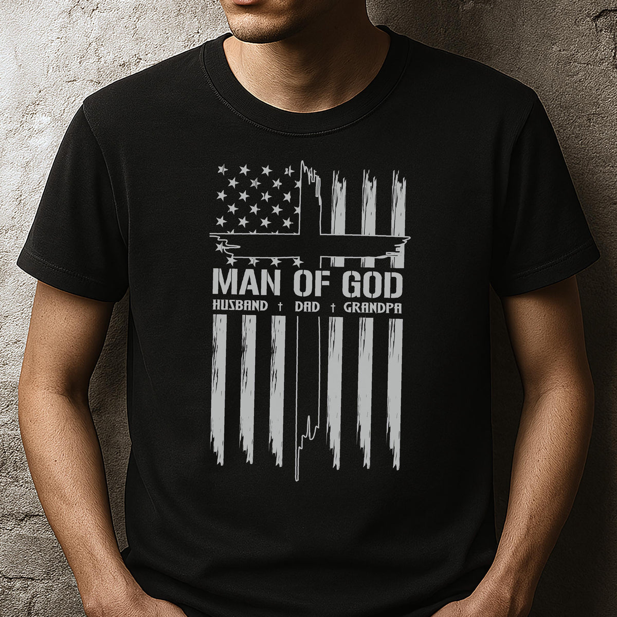 May include: Black t-shirt featuring a distressed American flag design with the text "MAN OF GOD" above "HUSBAND † DAD † GRANDPA" in white. The shirt has a crew neck and short sleeves.