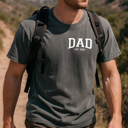 May include: A dark gray t-shirt with the word "DAD" in white letters and the text "EST. 2025" underneath.