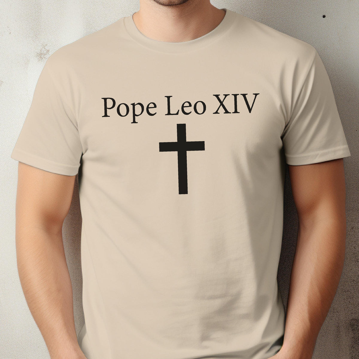 May include: Beige t-shirt with the text "Pope Leo XIV" above a black cross. The shirt is a short-sleeved crew neck style. The text and cross are centered on the front of the shirt.