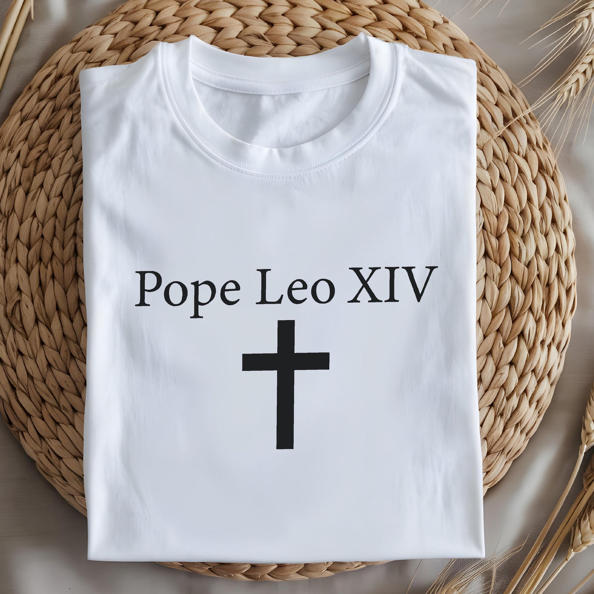 May include: White t-shirt with the text "Pope Leo XIV" above a black cross. The shirt is made of a soft material and is displayed on a woven surface.