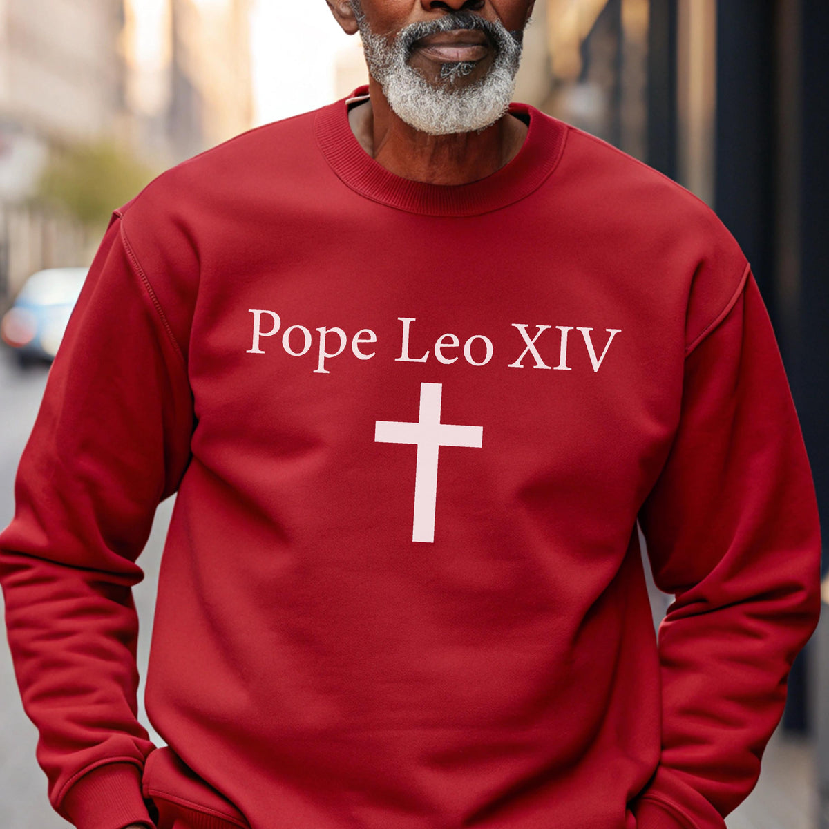 May include: A red sweatshirt with the text "Pope Leo XIV" above a white cross. The sweatshirt is a solid color and has long sleeves. The image is a close-up of the upper body.