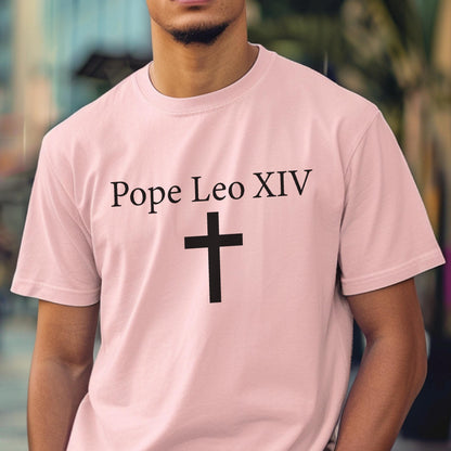 May include: A light pink t-shirt with the text "Pope Leo XIV" above a black cross. The shirt is a crew neck style and appears to be made of a soft material.