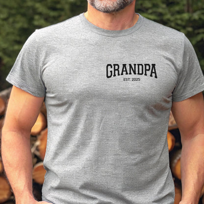 May include: A gray t-shirt with the word "GRANDPA" printed in black, with "EST. 2025" below it. The shirt is short-sleeved and appears to be made of a soft material.