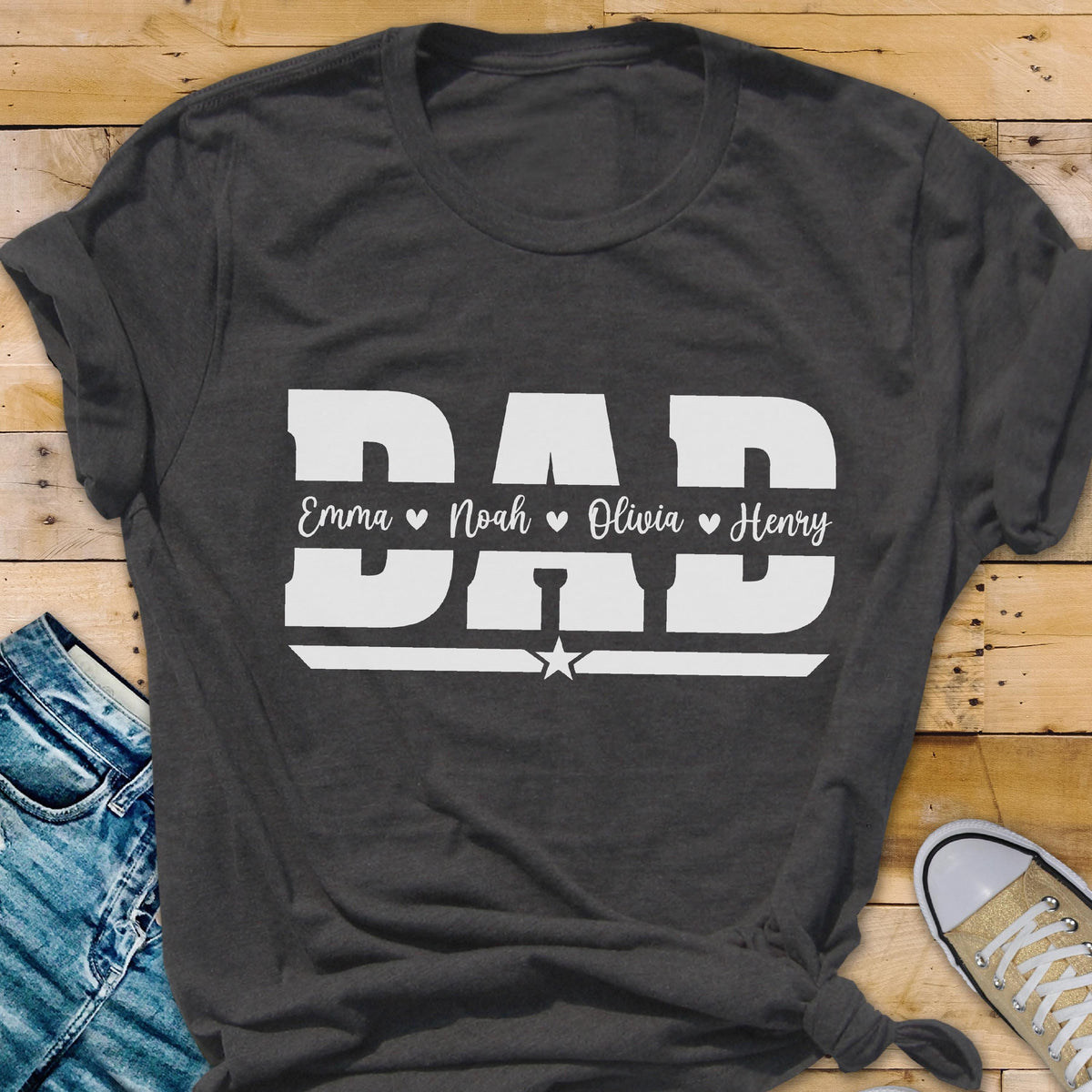 May include: Dark gray t-shirt with the word "DAD" in large white block letters. Below the word "DAD" are the names Emma, Noah, Olivia, and Henry. A white star is centered below the names.