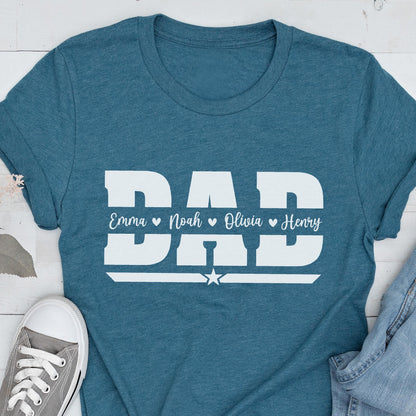 May include: Teal t-shirt with the word "DAD" in large white block letters. Below the word "DAD" are the names Emma, Noah, Olivia, and Henry. A white star is below the names. A gray sneaker and blue jeans are in the image.