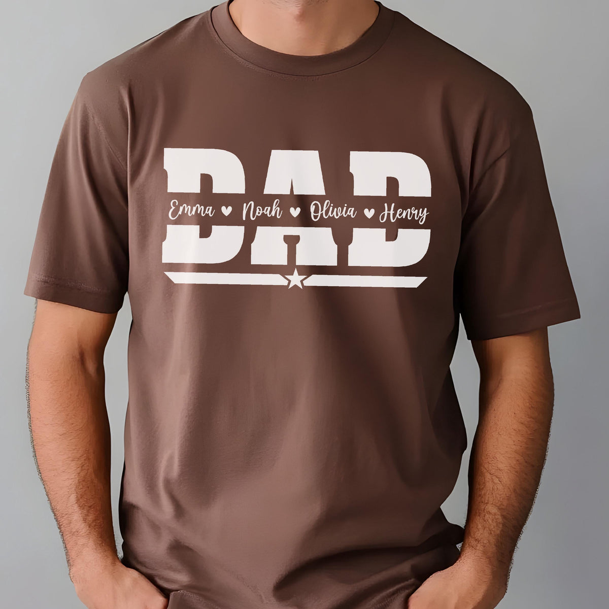 May include: A brown t-shirt with the word "DAD" in large white block letters. Below the word "DAD" are the names Emma, Noah, Olivia, and Henry, each separated by a heart symbol. A white star is centered below the names.