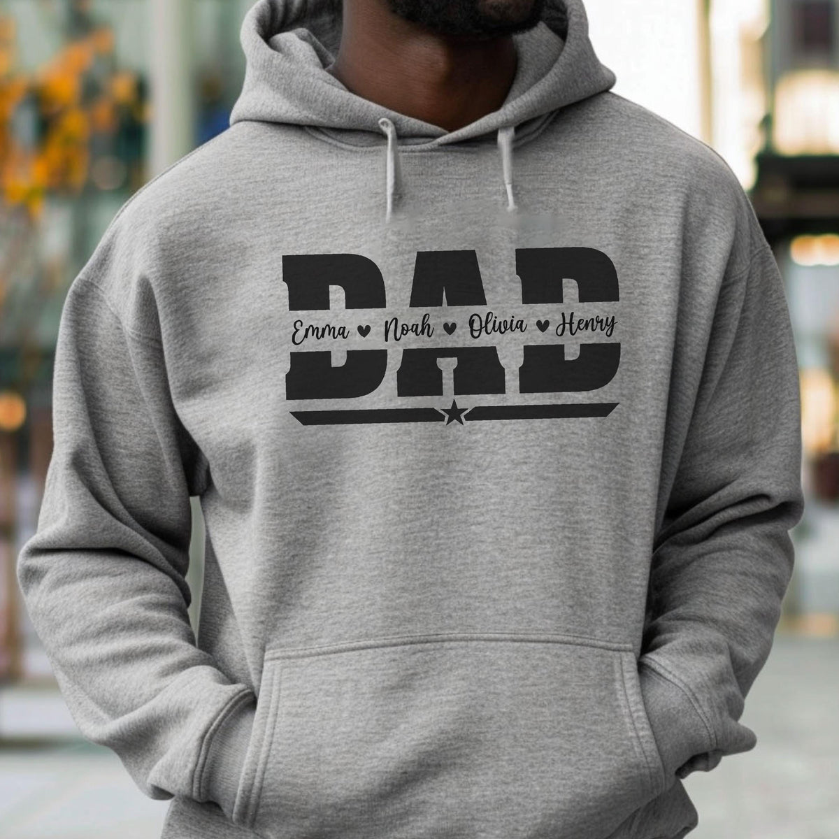 May include: A gray hoodie with the word "DAD" in bold, black letters. Below the word "DAD" are the names "Emma", "Noah", "Olivia", and "Henry", each with a heart symbol. A star is below the names.