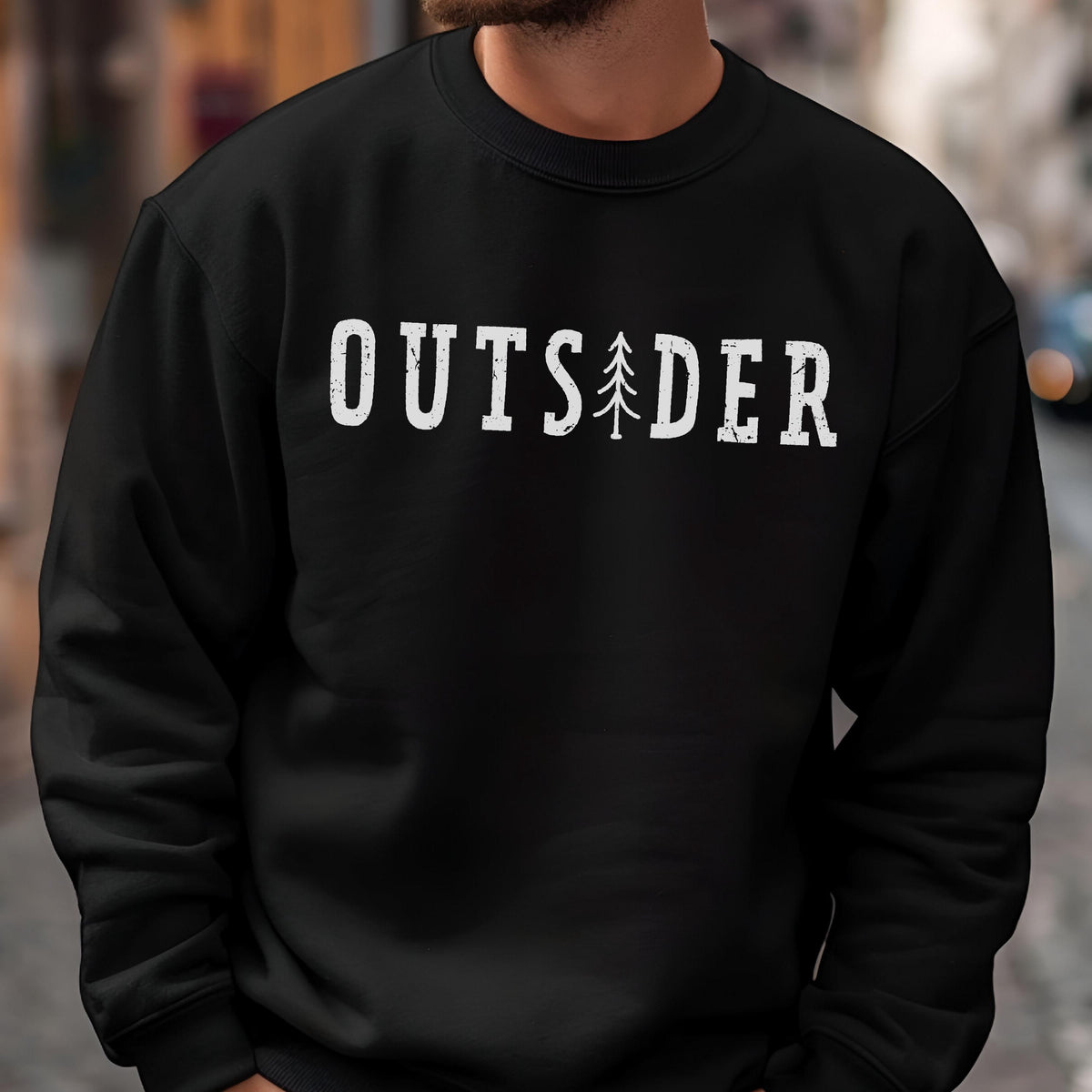 May include: A black crewneck sweatshirt featuring the white distressed text OUTSIDER printed across the chest, with a stylized pine tree graphic replacing the letter I. The garment has long sleeves and a ribbed collar, cuffs, and hem.