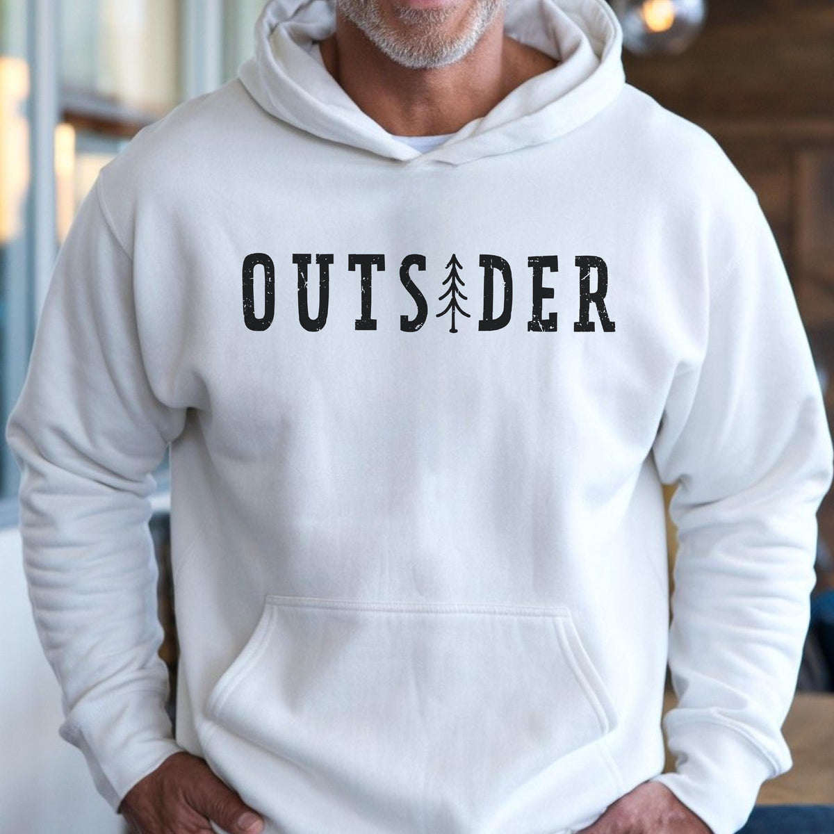 May include: A white long-sleeve hooded sweatshirt featuring a front kangaroo pocket. The chest displays the black text OUTSIDER in a distressed, block-style font, with a stylized pine tree graphic replacing the letter I in the word.