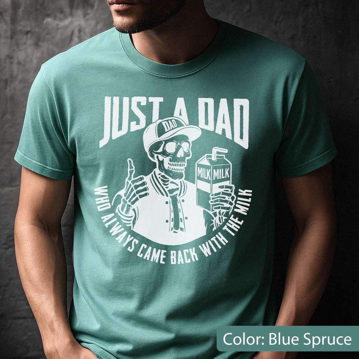 May include: Blue spruce t-shirt with a white graphic. The graphic features a skeleton wearing a baseball cap and jacket, holding a milk carton and giving a thumbs up. Text reads "JUST A DAD" and "WHO ALWAYS CAME BACK WITH THE MILK."