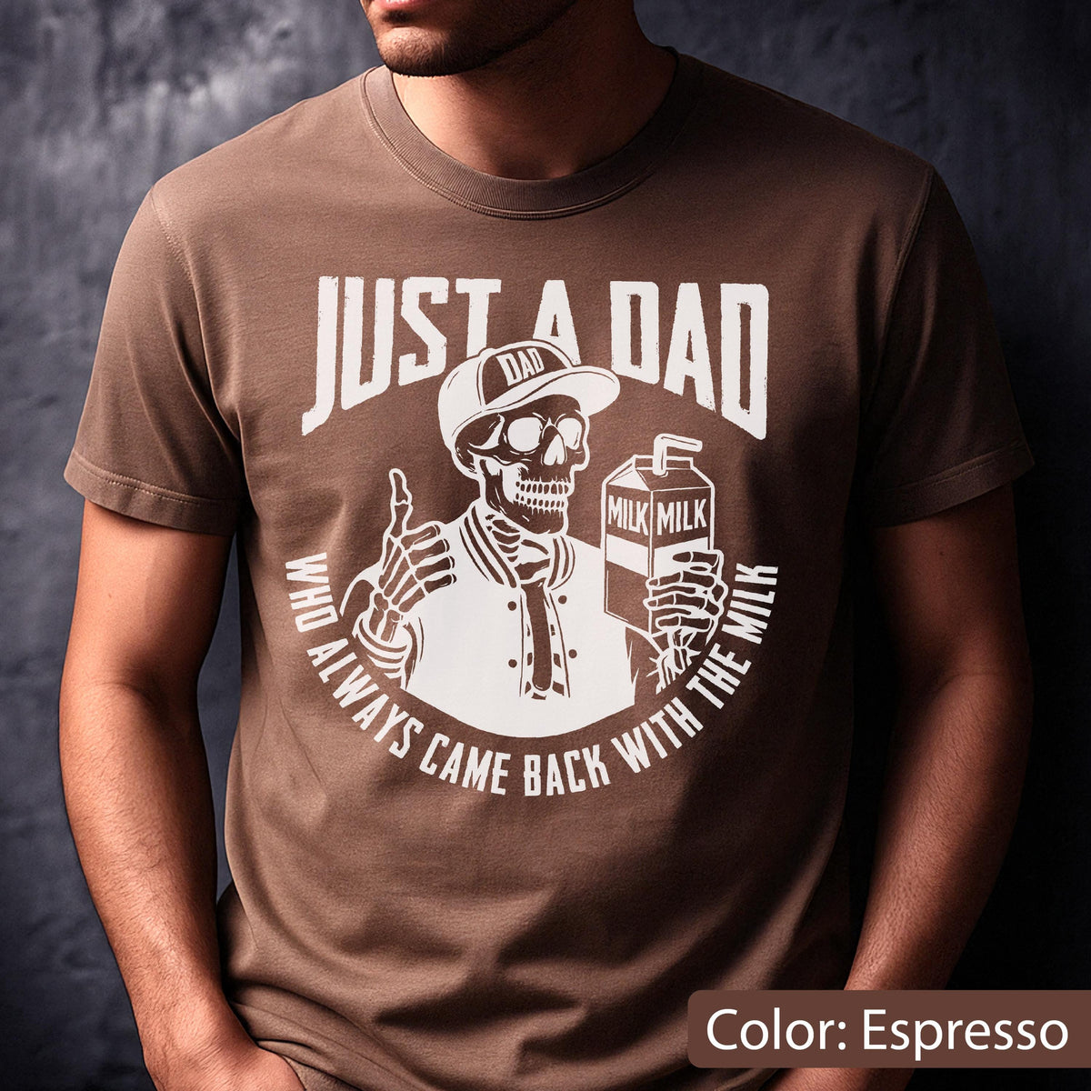 May include: Espresso-colored t-shirt featuring a white graphic of a skeleton wearing a baseball cap that says "DAD" and holding a milk carton. The text "JUST A DAD" is above the skeleton, and "WHO ALWAYS CAME BACK WITH THE MILK" is below.