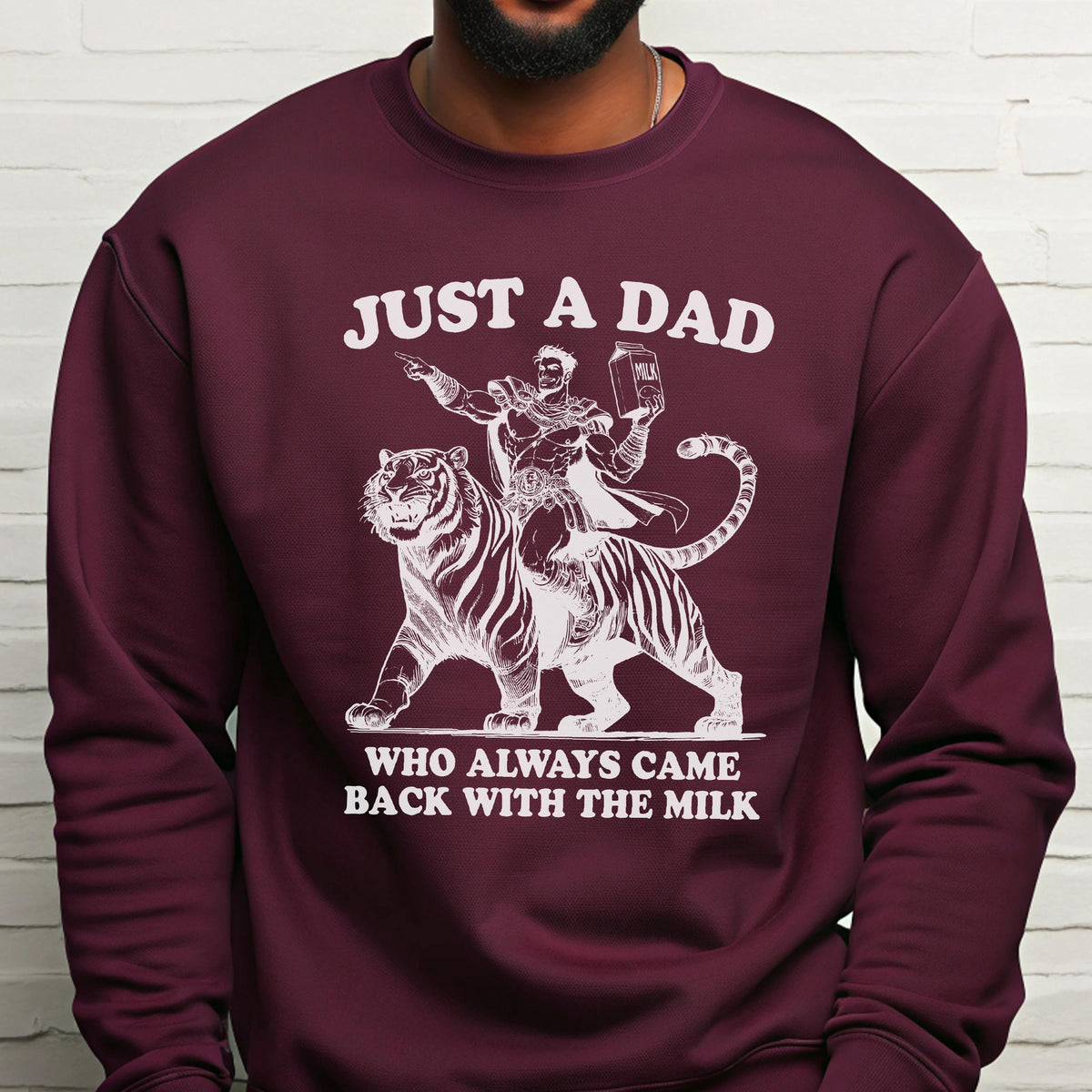 May include: Burgundy sweatshirt with a white graphic of a man riding a tiger, holding a milk carton. Text reads "JUST A DAD" above the image and "WHO ALWAYS CAME BACK WITH THE MILK" below.