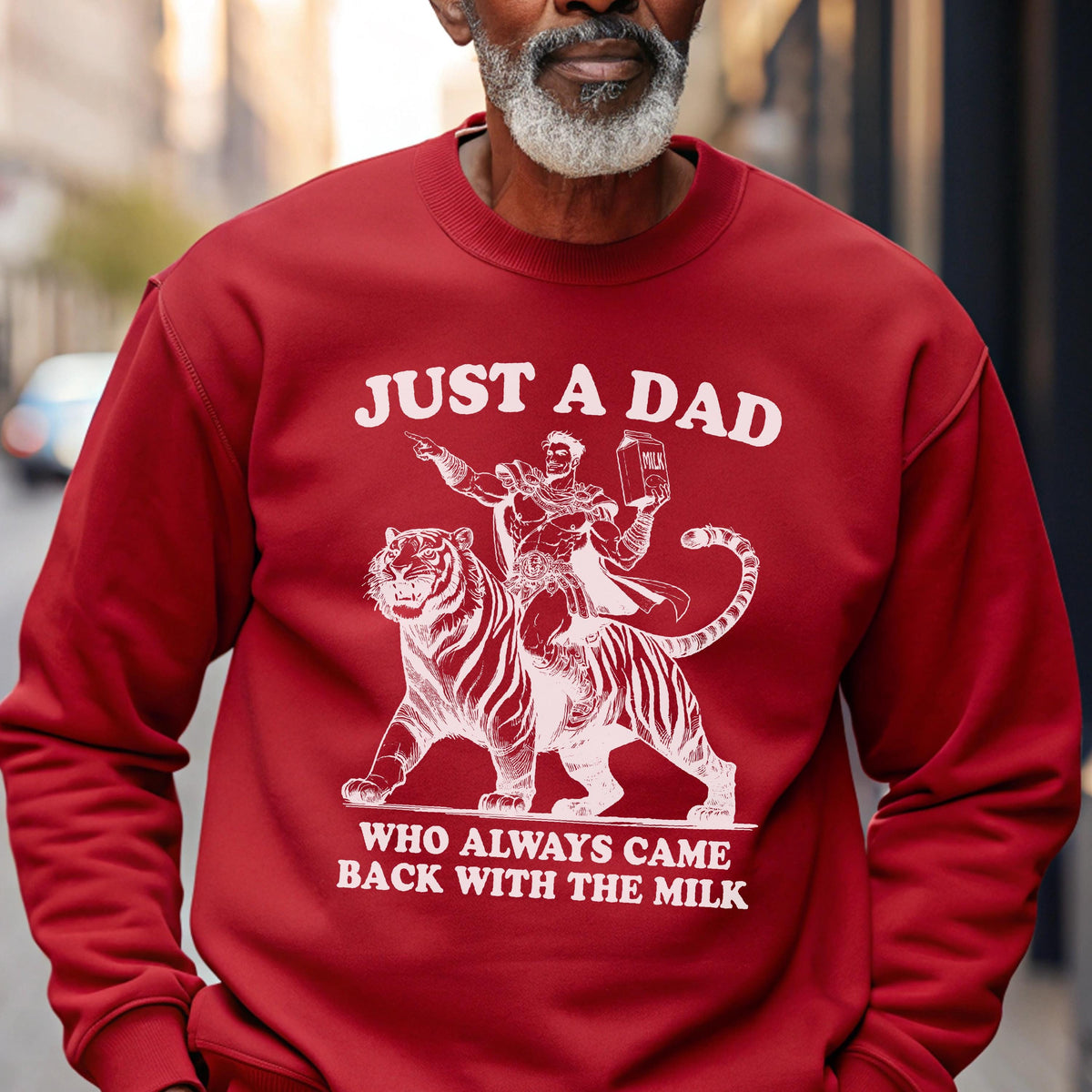 May include: Red sweatshirt with a white graphic of a superhero riding a tiger, holding a milk carton. The text reads "JUST A DAD WHO ALWAYS CAME BACK WITH THE MILK."