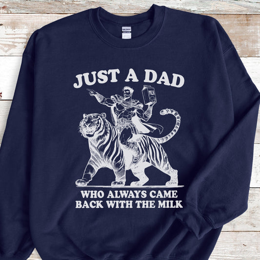May include: Navy blue sweatshirt with a white graphic. The graphic features a superhero riding a tiger, holding a milk carton, and the text "JUST A DAD WHO ALWAYS CAME BACK WITH THE MILK."