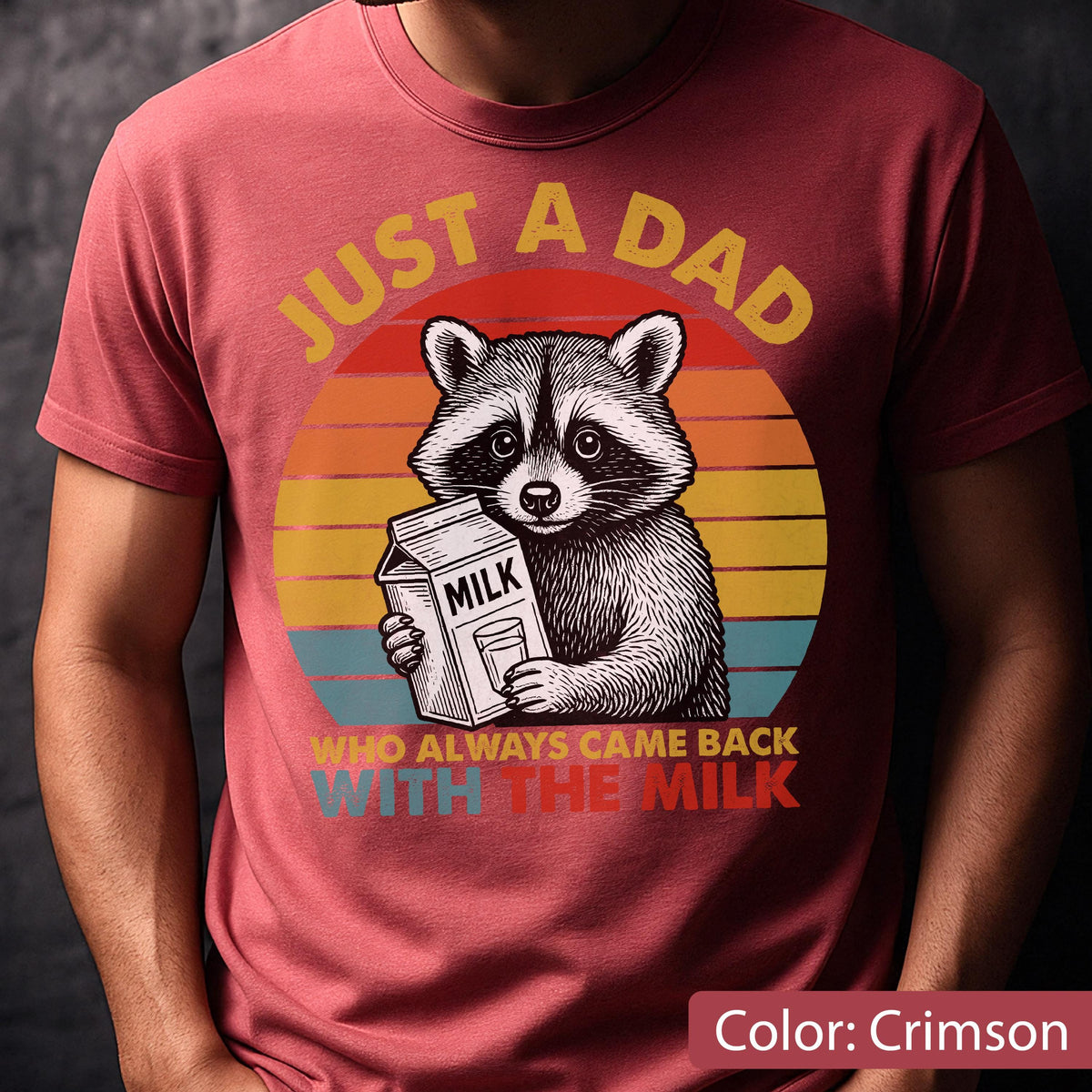 May include: Crimson t-shirt featuring a raccoon holding a milk carton, with the text "JUST A DAD WHO ALWAYS CAME BACK WITH THE MILK" in a retro sunset design. The shirt is a comfortable fit.