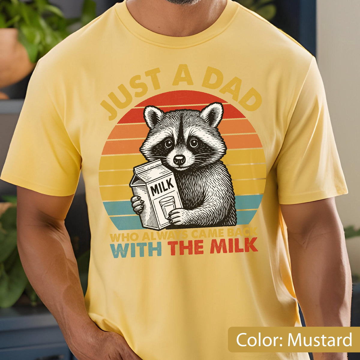 May include: Mustard yellow t-shirt featuring a raccoon holding a milk carton. The design includes the text "JUST A DAD WHO ALWAYS CAME BACK WITH THE MILK" in a retro sunset style.
