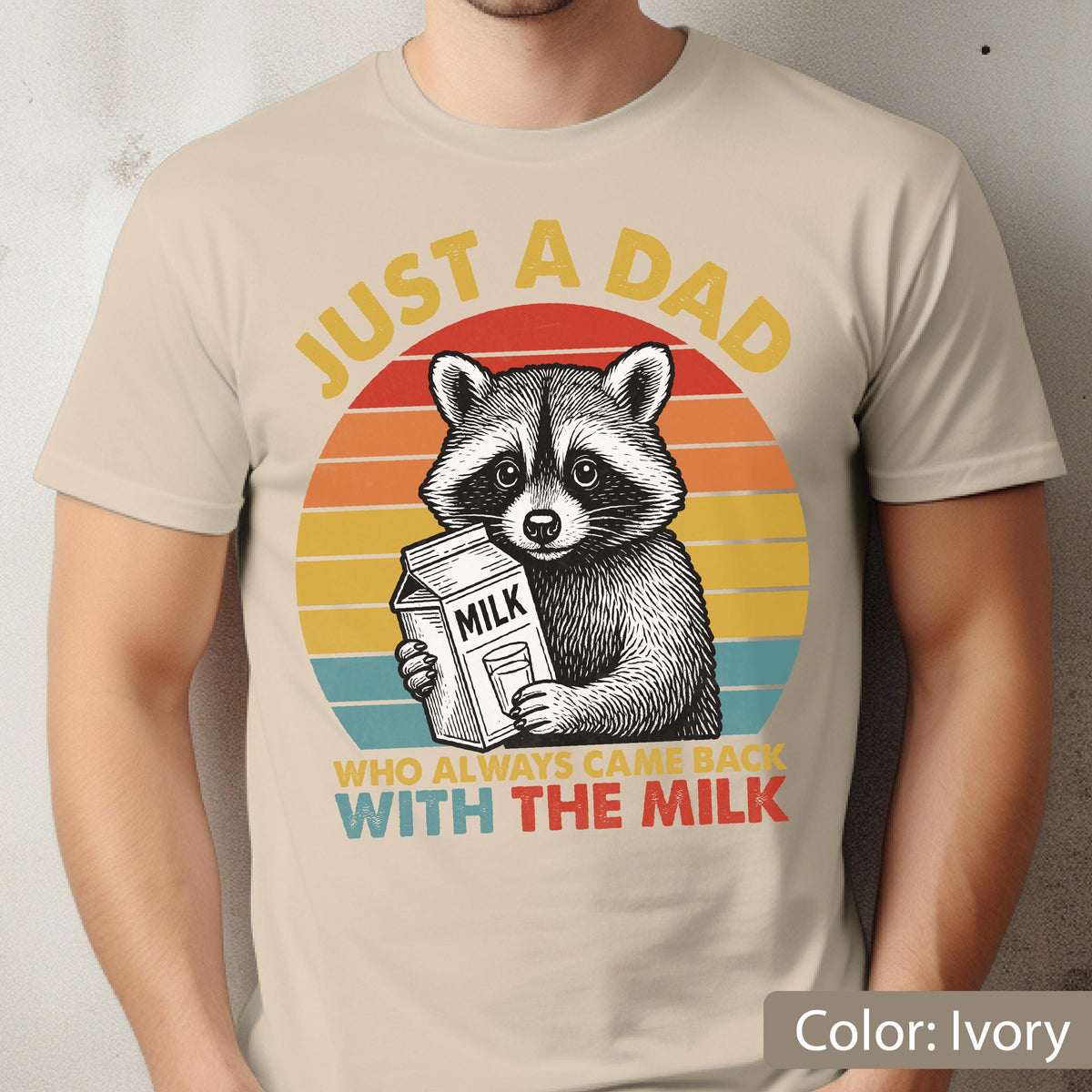 May include: Ivory-colored t-shirt featuring a raccoon holding a milk carton, set against a retro sunset design. Text reads "JUST A DAD WHO ALWAYS CAME BACK WITH THE MILK". The shirt is a comfortable, casual wear item.