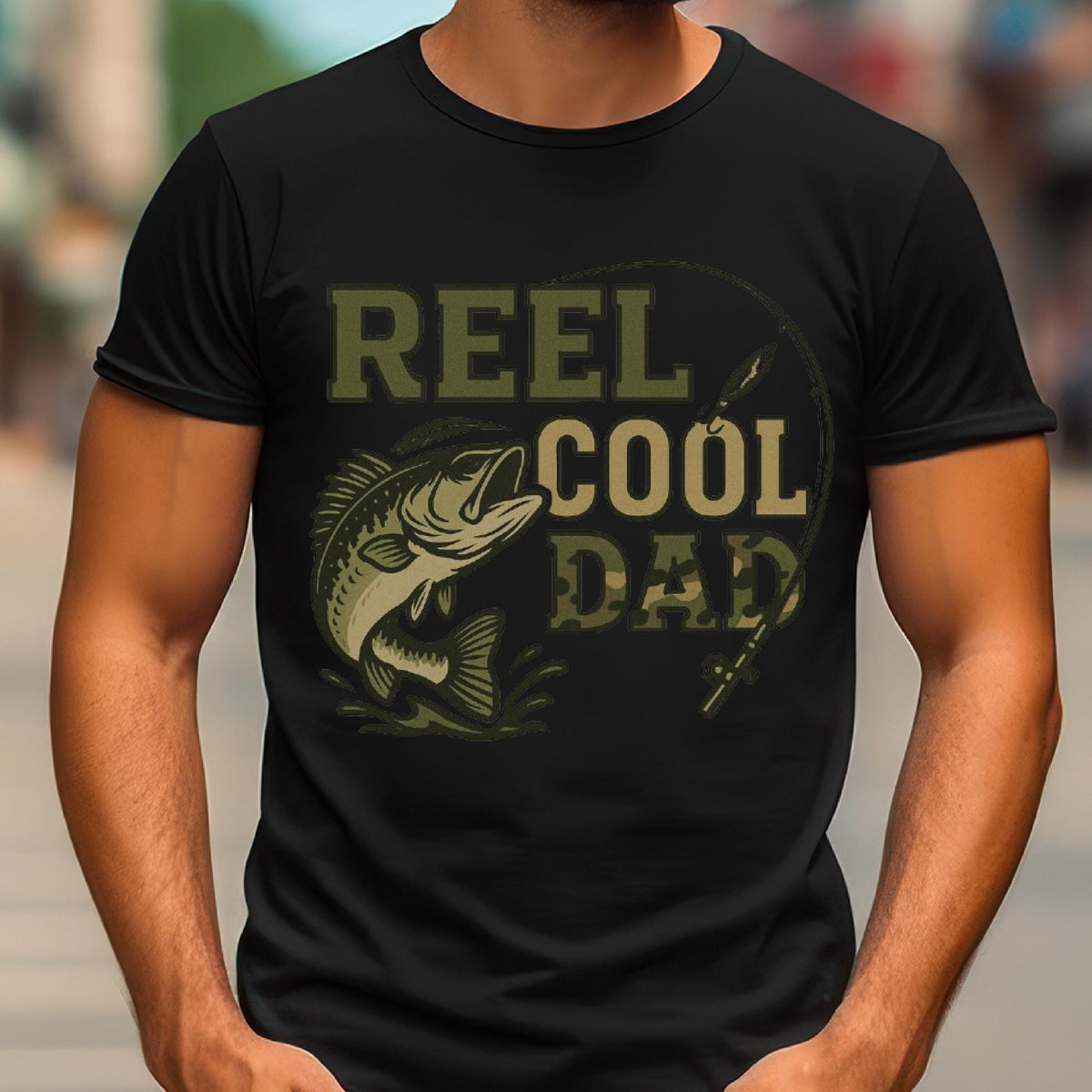 May include: A black short-sleeved t-shirt featuring a graphic print in olive green and camouflage tones. The design includes a fish illustration, a fishing rod, and the text REEL COOL DAD printed in a bold, block-style font across the chest area.